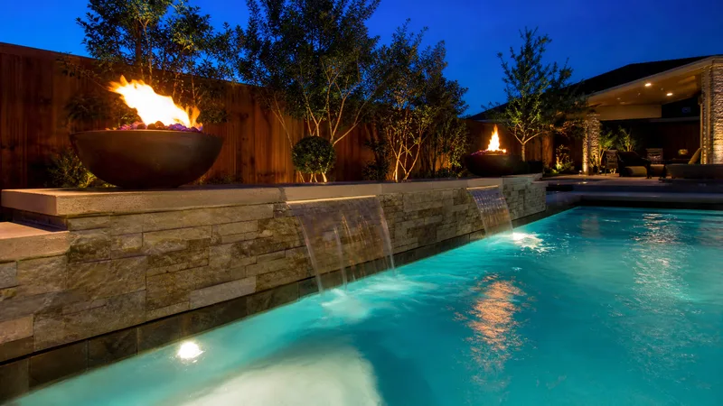 Sheer descent waterfall and fire bowls on a custom Houston pool at dusk